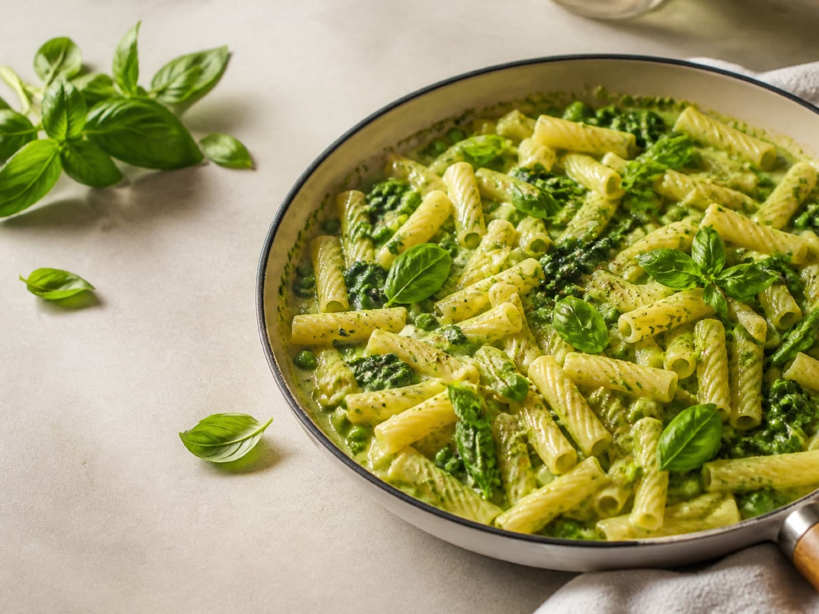 Creamy pesto pasta with peas, spinach, and basil in a skillet